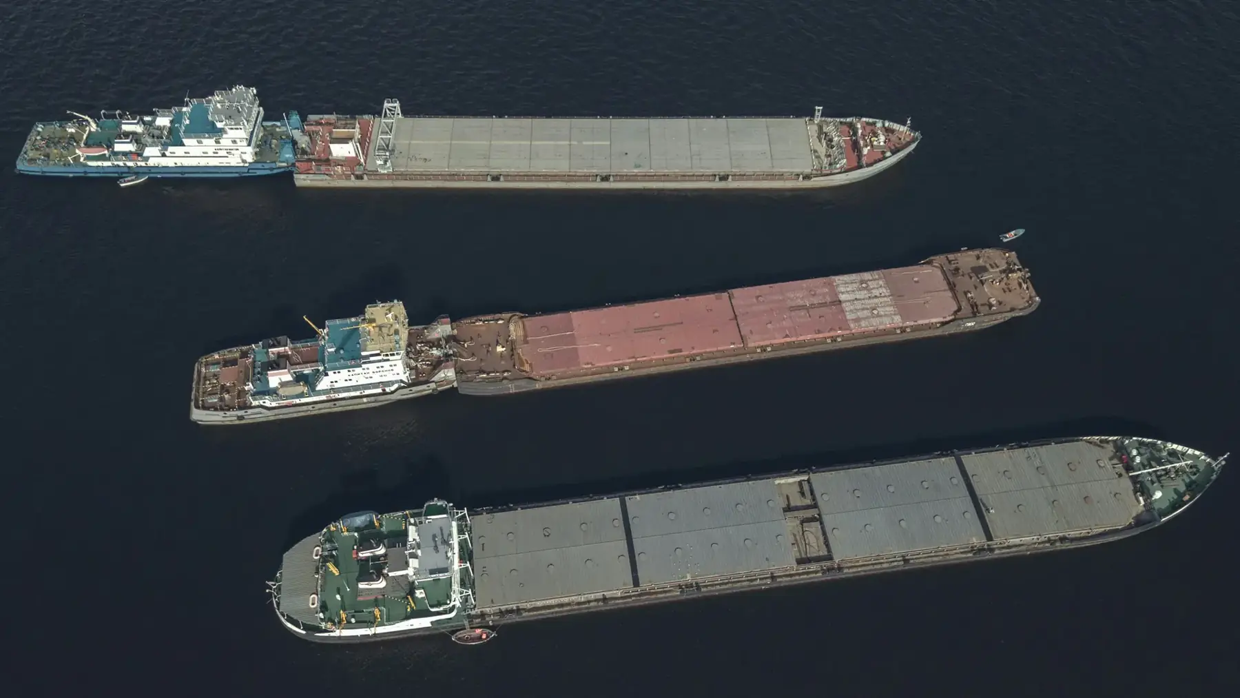Three cargo barges seen from above on dark water